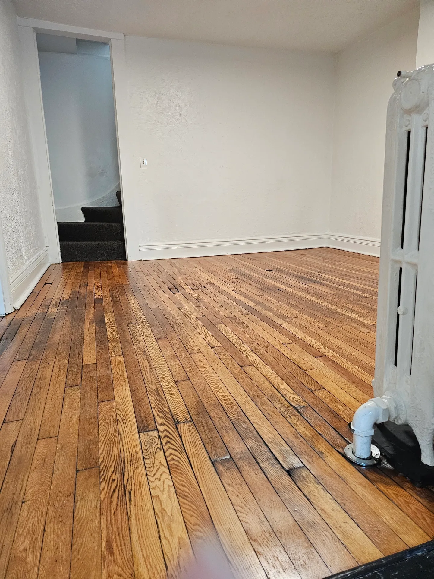 Empty room with wooden floor and radiator.