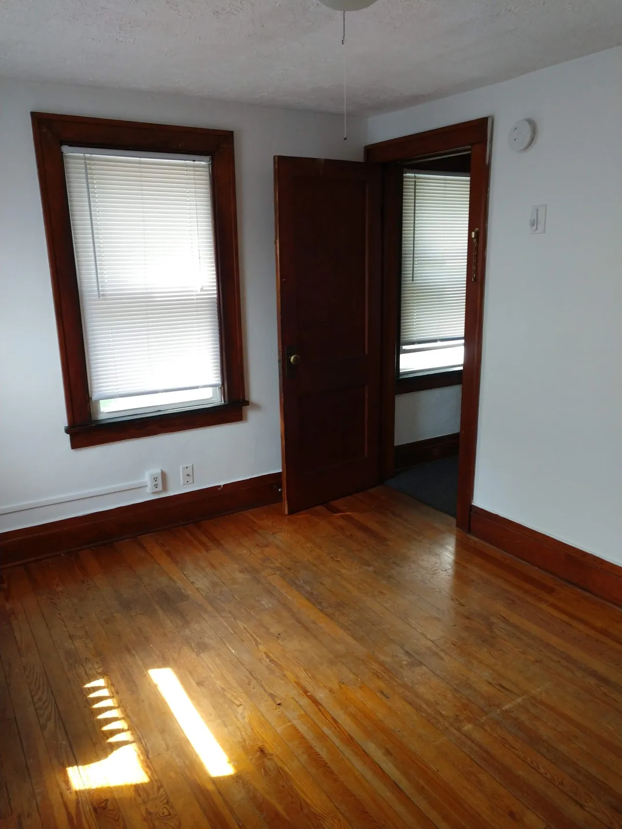 Empty room with wooden floor and blinds.