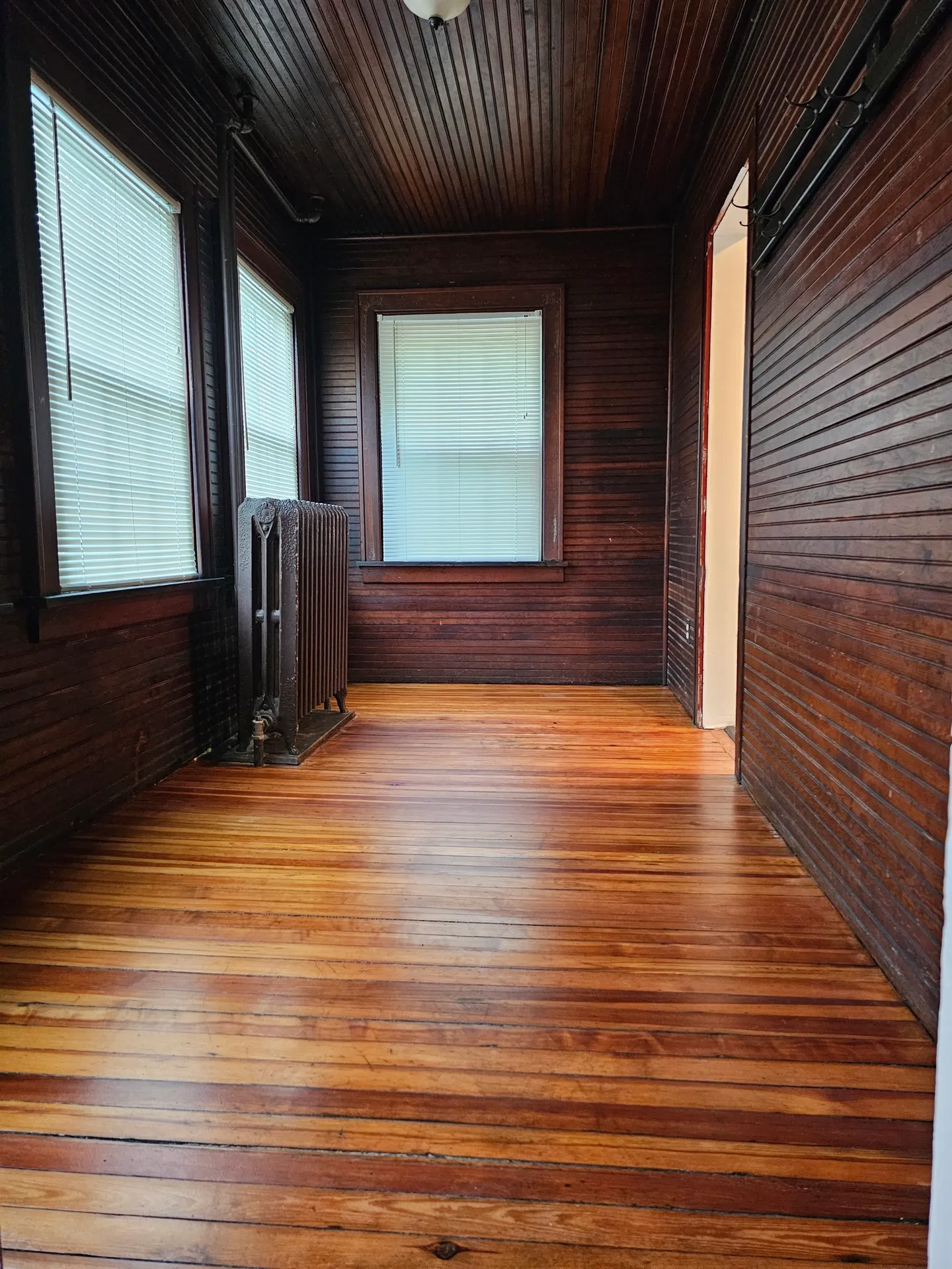 Wood-paneled room with wooden floor and windows.