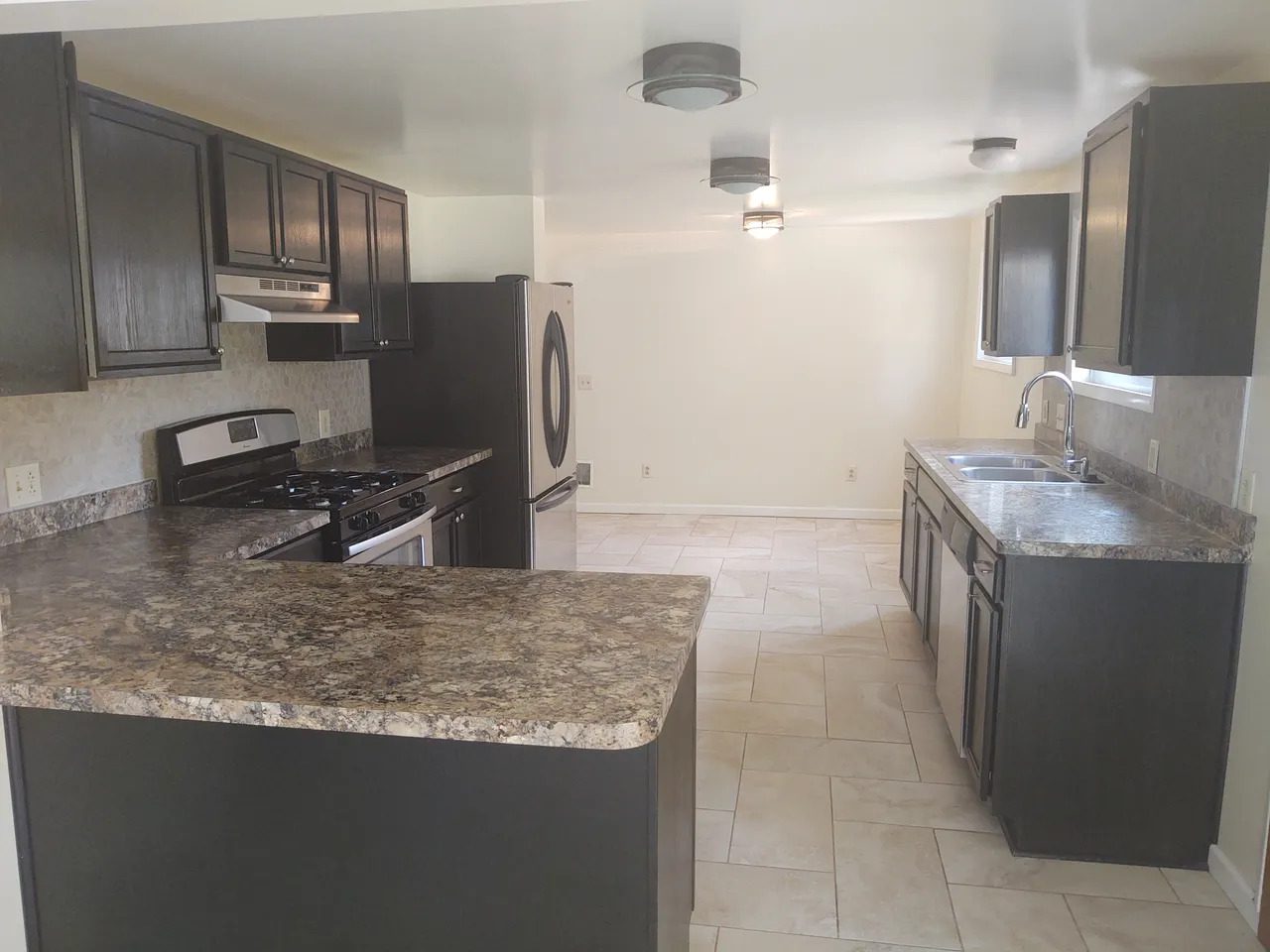 A kitchen with black cabinets and white tile floors.